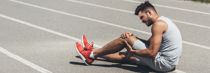 A man sitting on a running track holding his knee, appearing to be in pain